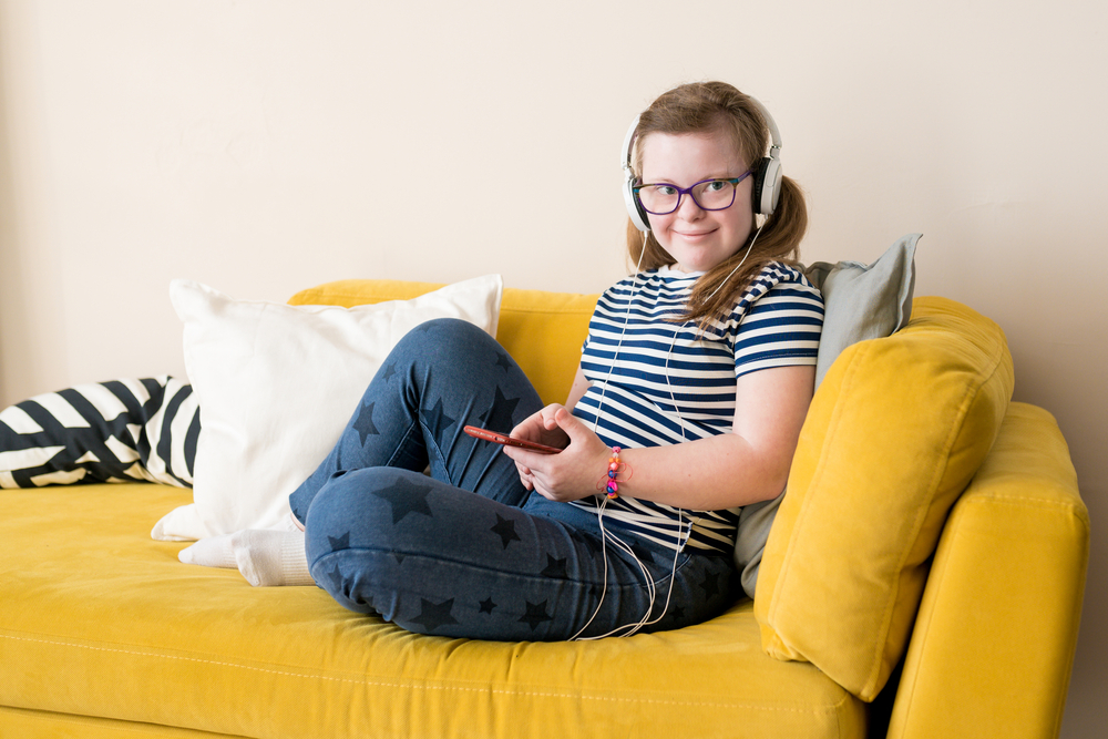 Jente med downs-syndrom, sittende på en gul sofa, hører på musikk. Foto