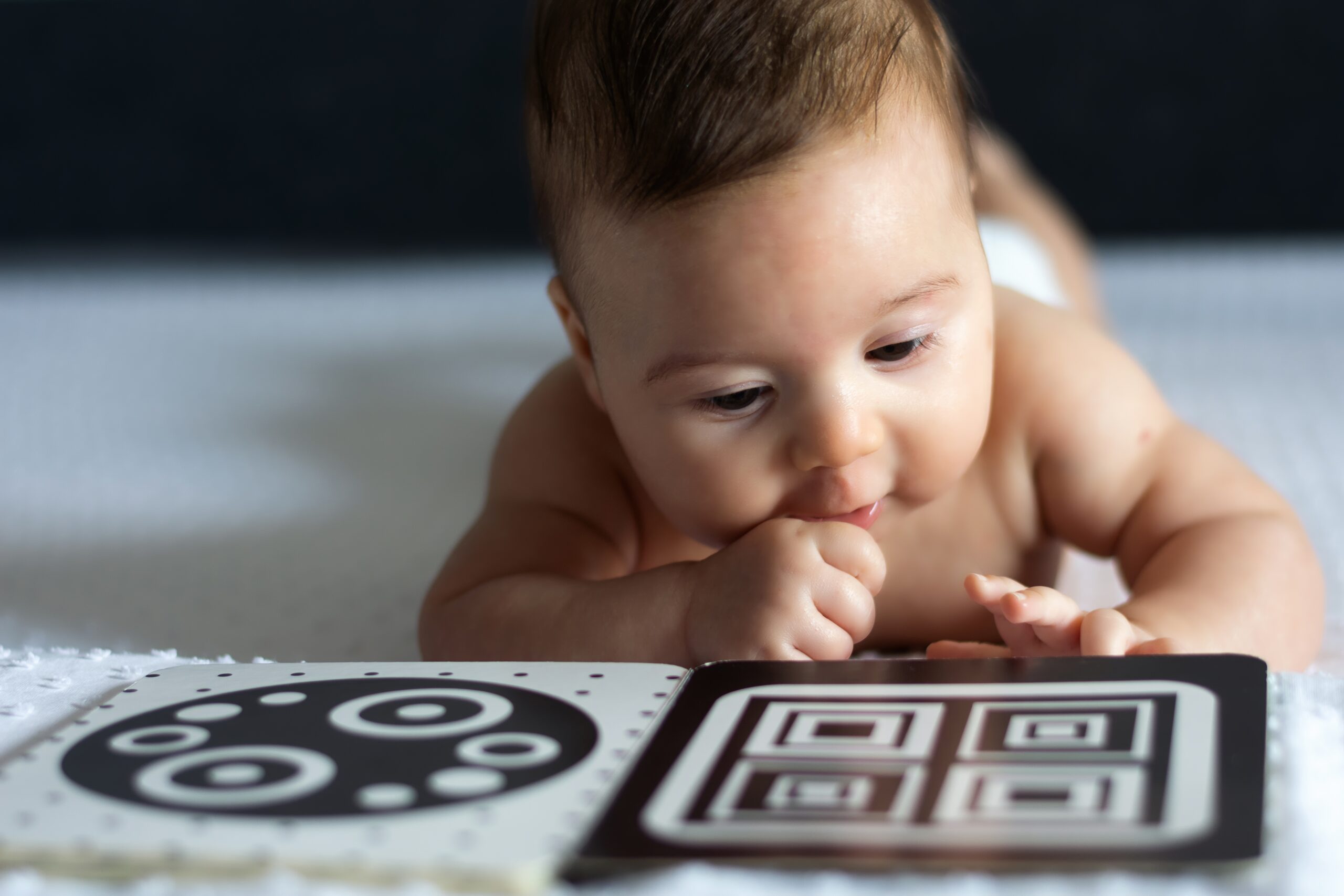 Baby ligger på magen og titter på en bok. Foto
