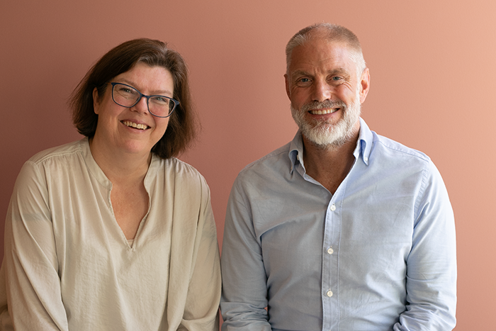 Ruth Aga og Mikkel Pretorius sittende foran en oransje vegg. Foto