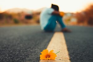 Orange blomst ligger på veien, og vi ser en jente i bakgrunnen. Fargen er fargen som markerer selvmordsforebygging.