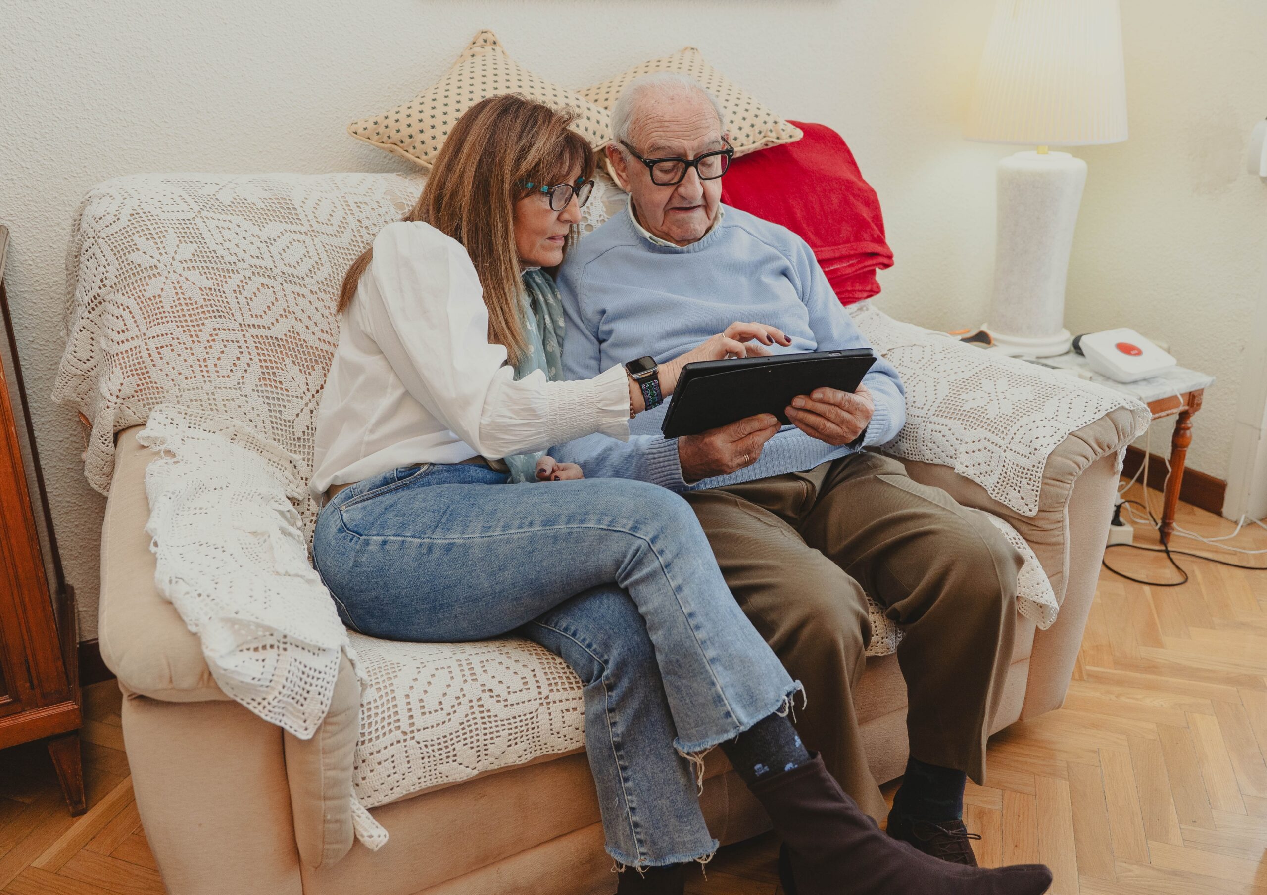 Datter og eldre mann sitter i sofa og ser på en tablet sammen. Foto